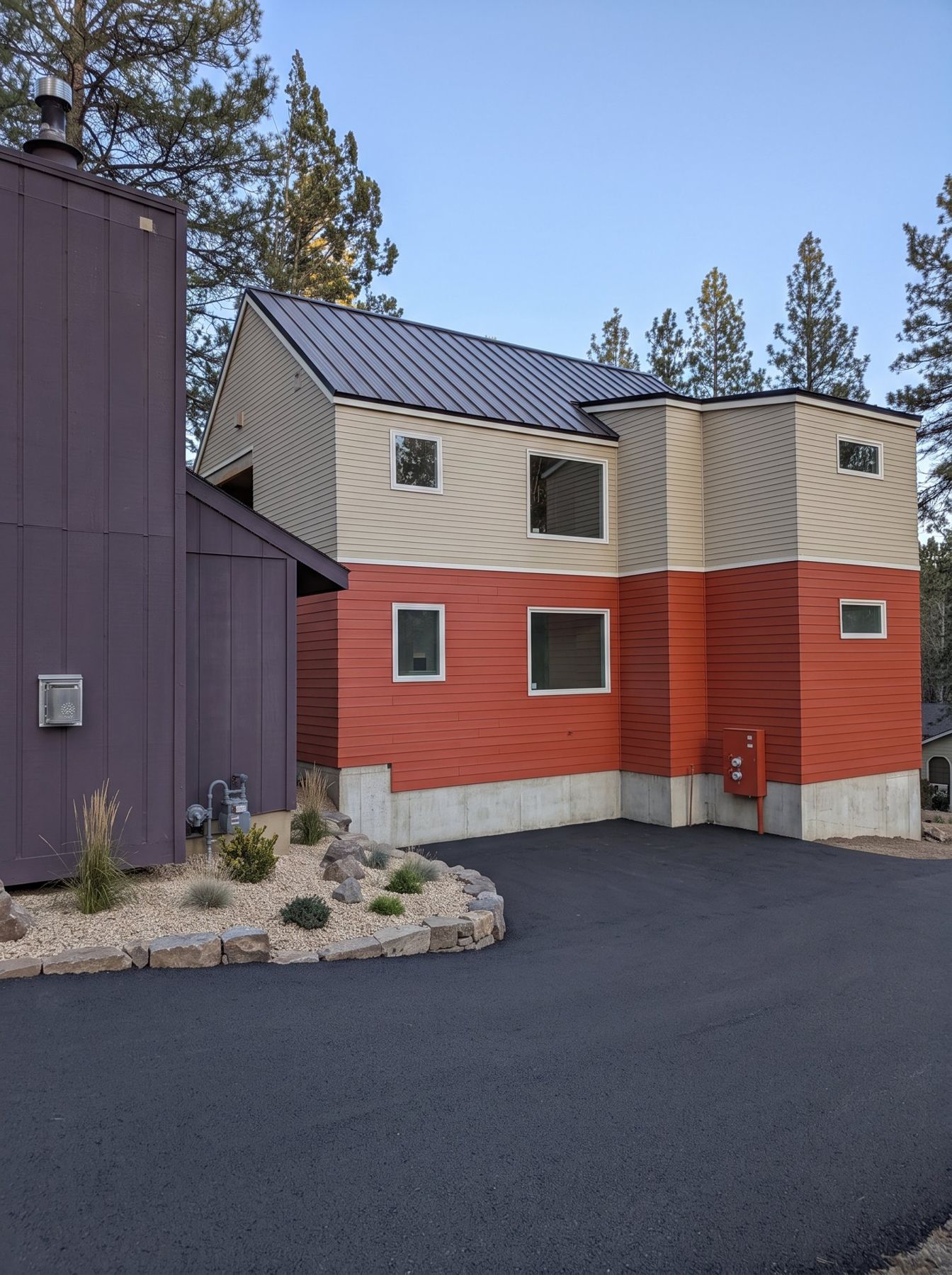 Finished two-story ADU with red and tan lap siding, standing-seam metal roof and a new paved driveway