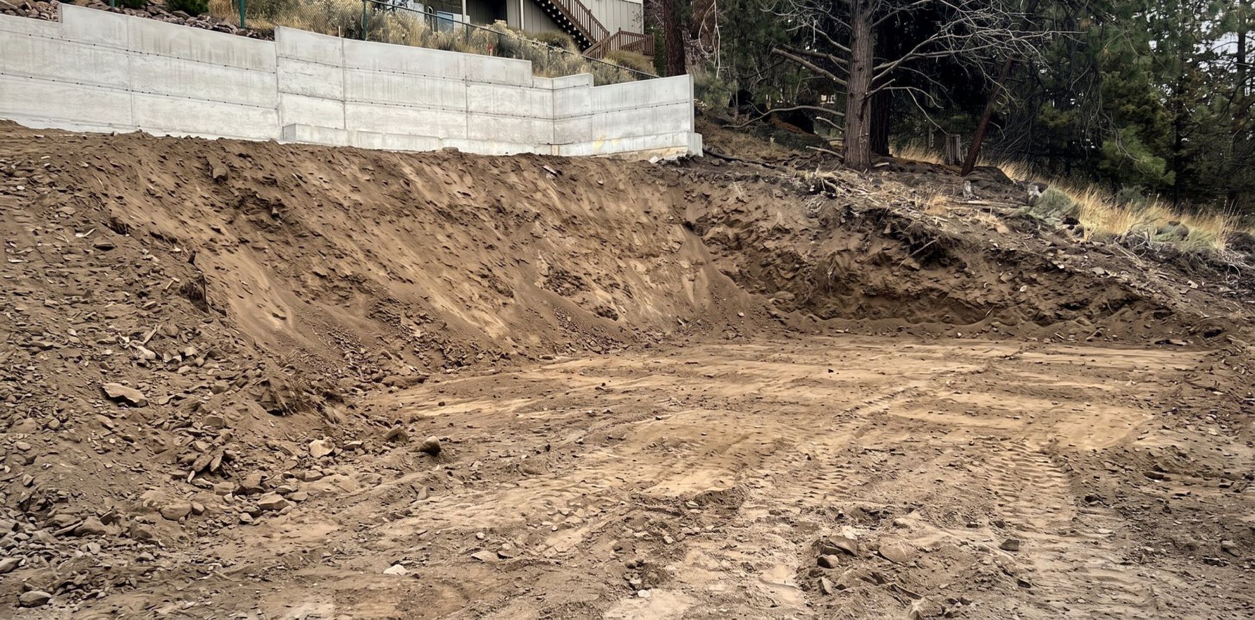 Excavated and graded building pad below a new concrete retaining wall on a Bend lot